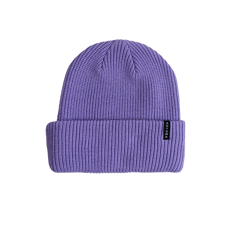 A purple ribbed knit beanie hat with a folded cuff, featuring a small black brand tag on the side, set against a plain white background.