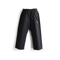 Black wide-leg snow pants with an elastic waistband and a small orange circular logo on the upper left thigh, shown against a plain white background.