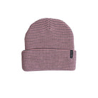 A pink and black checkered knit beanie hat with a folded cuff and a small black brand tag on the side, shown against a plain white background.