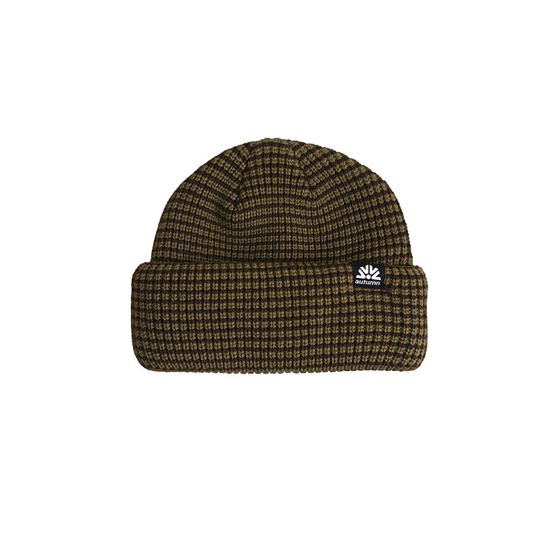 A ribbed knit beanie hat in a dark brown and black micro-check pattern, featuring a small white embroidered logo patch on the front cuff.