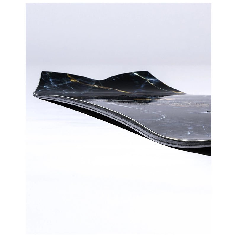 A close-up of a skateboard deck showing its black and dark gray marble-look graphic with subtle gold veining, photographed on a clean white studio background.