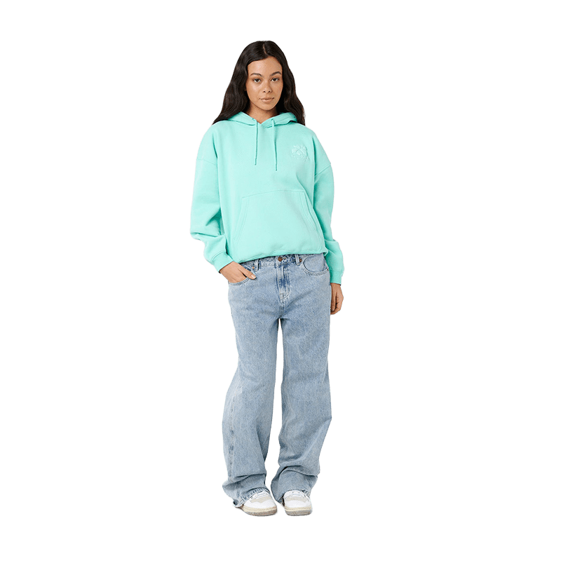 A model stands against a solid white background wearing a light mint green hoodie with a small white graphic on the left chest, paired with light-wash blue jeans and white sneakers.