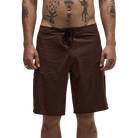 A man wearing brown board shorts with a black drawstring waist, shown from the chest down against a plain white background.