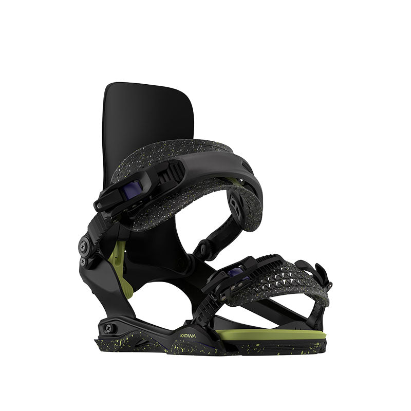 A single snowboard binding shown on a plain white background. The binding is primarily black with textured black straps, a light olive green baseplate, and small yellow-green speckles, plus small purple accents on the adjustment dials.