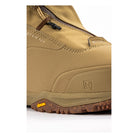 Close-up of a tan leather boot with a brown textured sole, showing the side zipper, embossed logo, and a small yellow Vibram badge on the outsole.