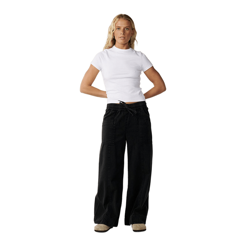 A woman modeling a white short-sleeve mock neck crop top and black wide-leg drawstring pants against a solid white background.